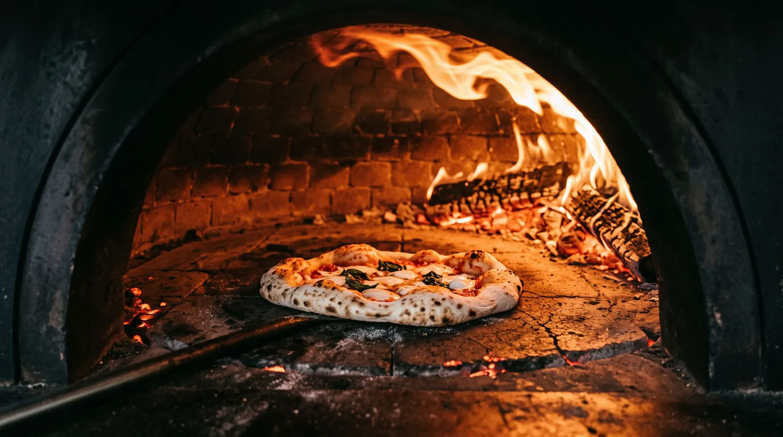 Pizza posée sur la sole incandescente d'un four à bois, flamme léchant la voûte